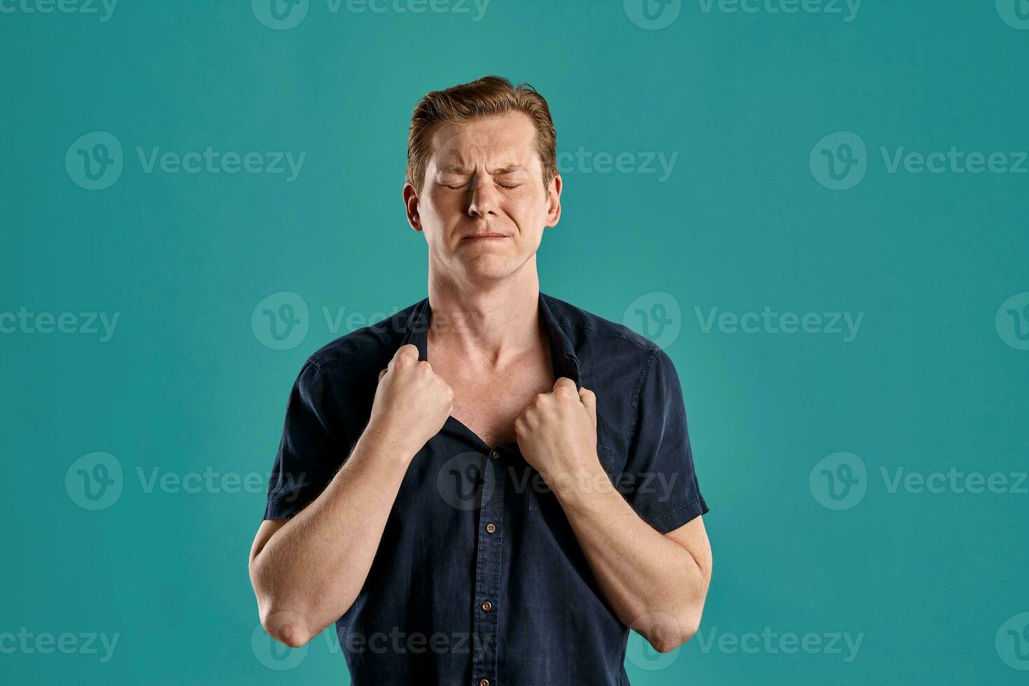 Close-up portrait of a ginger guy in navy t-shirt posing on blue background. Sincere emotions. photo