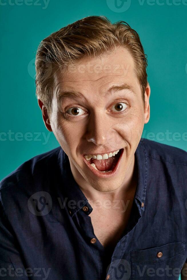 Close-up portrait of a ginger guy in navy t-shirt posing on blue background. Sincere emotions. photo