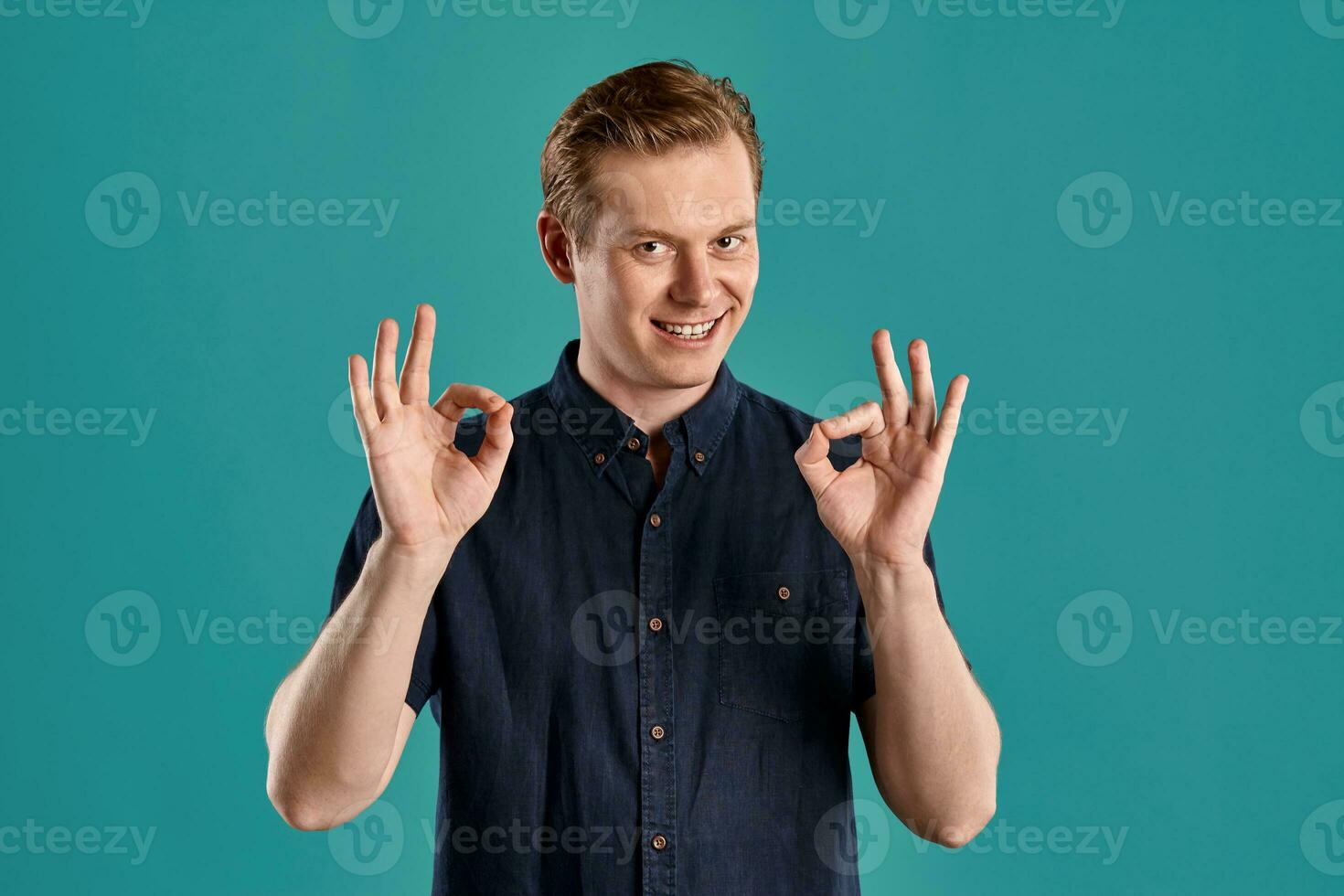 Close-up portrait of a ginger guy in navy t-shirt posing on blue background. Sincere emotions. photo