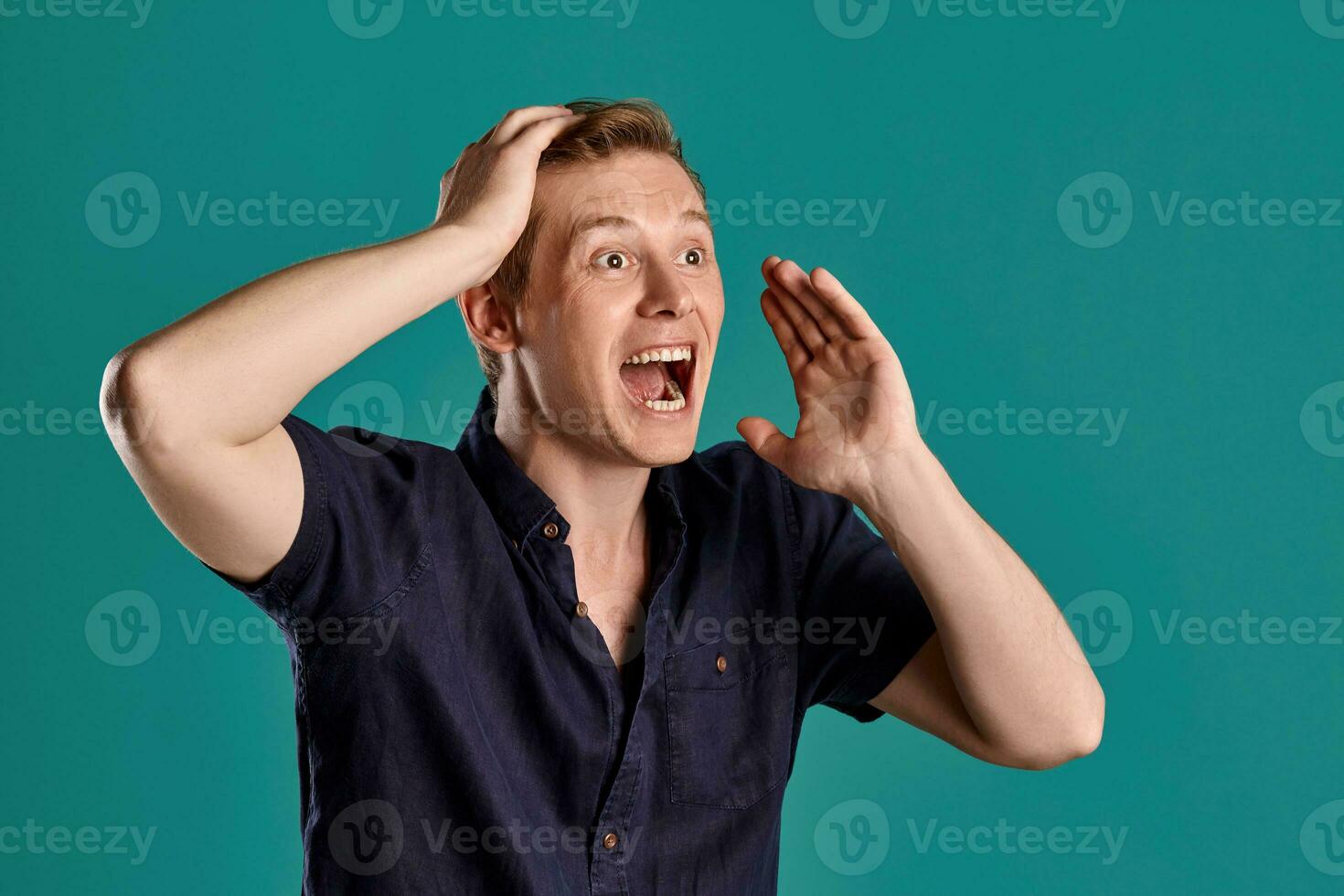 Close-up portrait of a ginger guy in navy t-shirt posing on blue background. Sincere emotions. photo