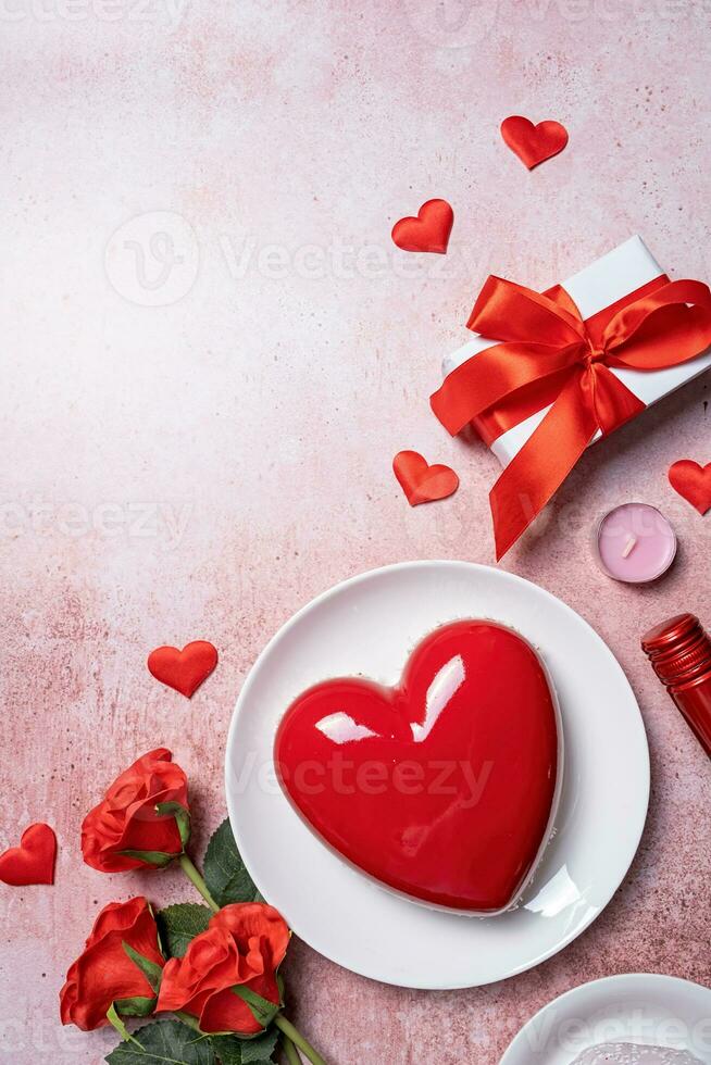 heart shaped glazed valentine cake, gift and wine on pink concrete background photo