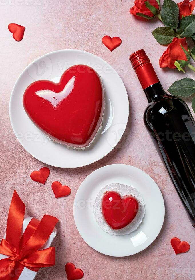 heart shaped glazed valentine cake, gift and wine on pink concrete background photo