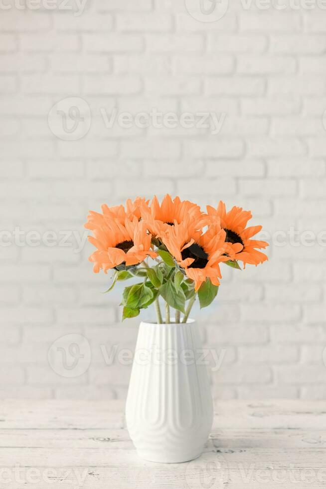 Color of the year 2024, Peach Fuzz. A bouquet of sunflowers in a vase against the background of a white brick wall. Copy space for text. photo