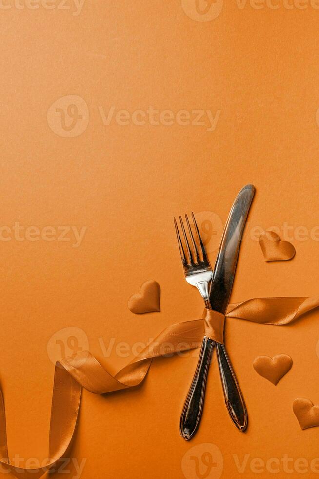 Color of the year 2024, Peach Fuzz.  Fork and knife tied with a red ribbon in a shape of heart rate on red background photo