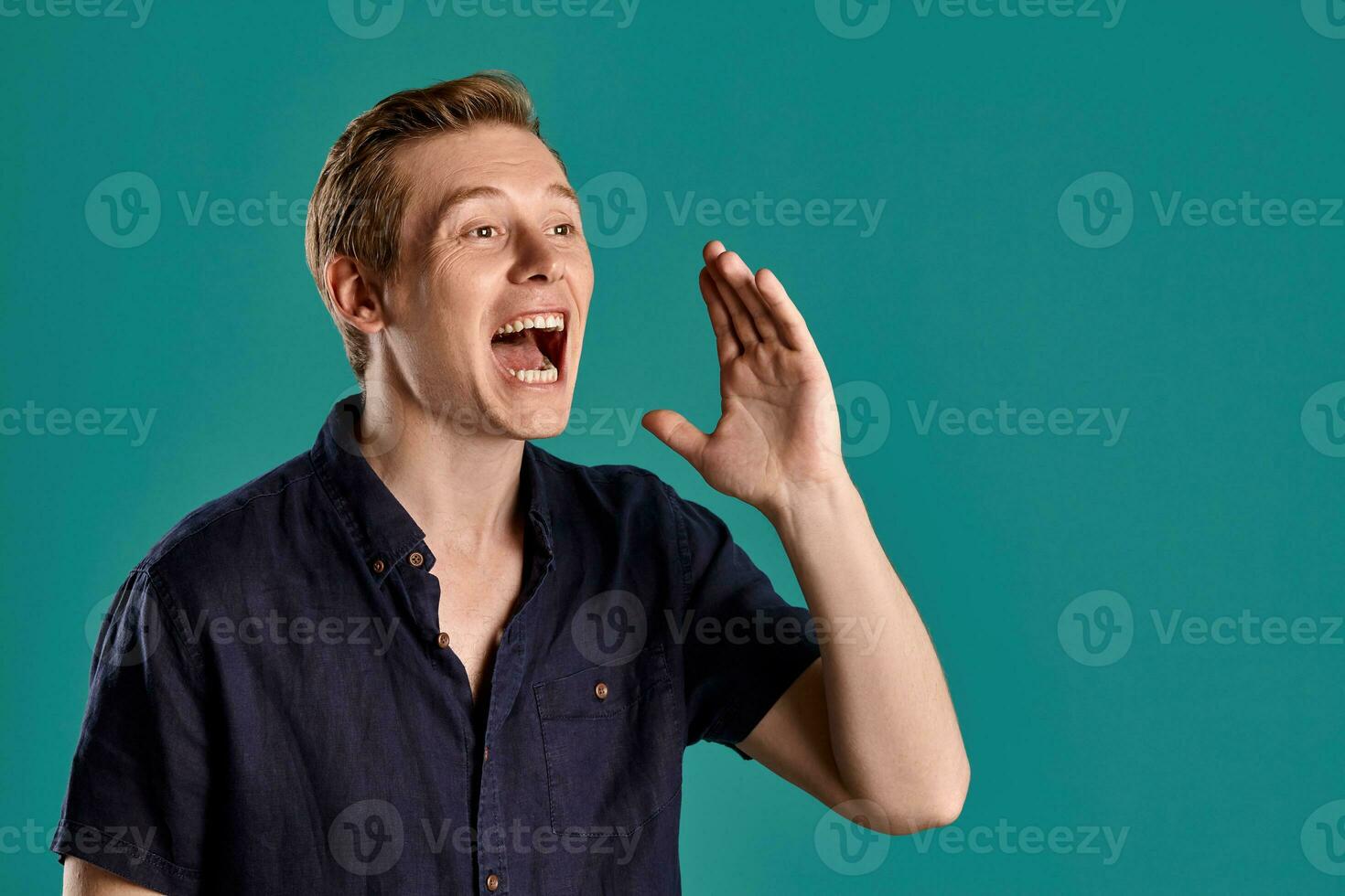 Close-up portrait of a ginger guy in navy t-shirt posing on blue background. Sincere emotions. photo