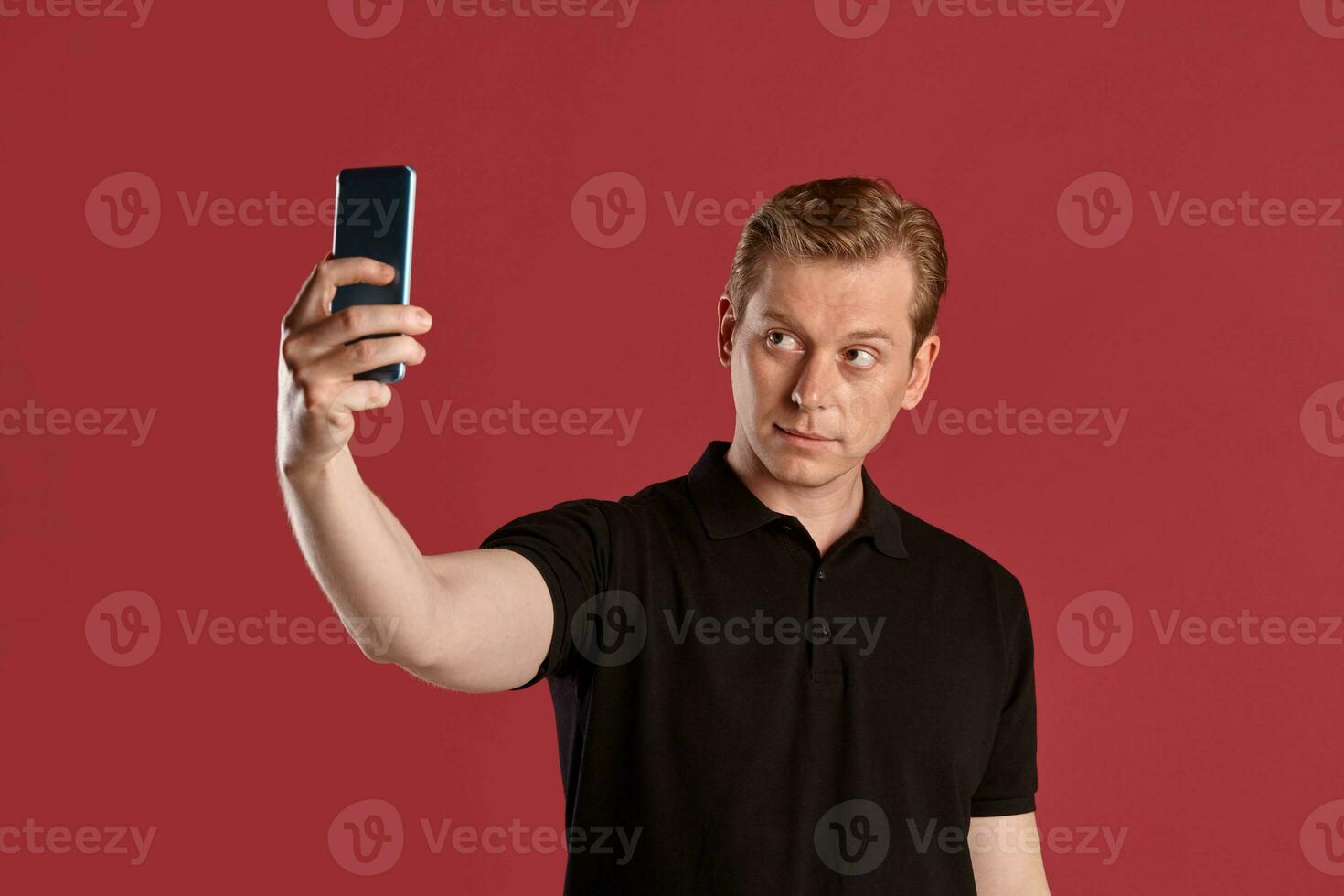 de cerca retrato de un jengibre chico en negro camiseta posando en rosado antecedentes. sincero emociones foto