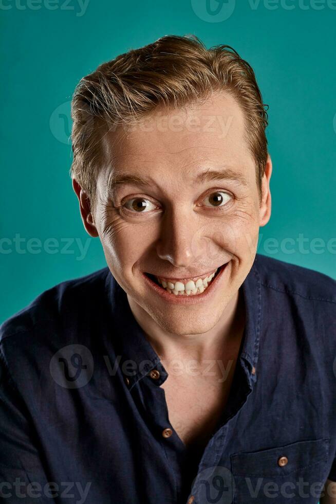 Close-up portrait of a ginger guy in navy t-shirt posing on blue background. Sincere emotions. photo