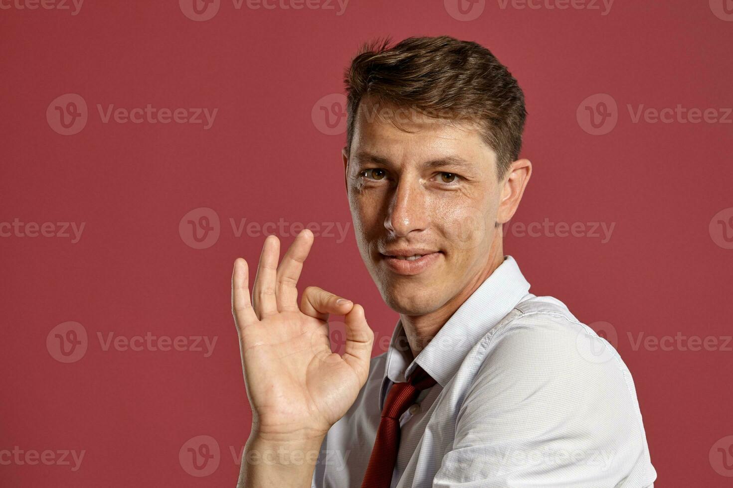 Young man in a classic white shirt and red tie posing over a pink background. photo