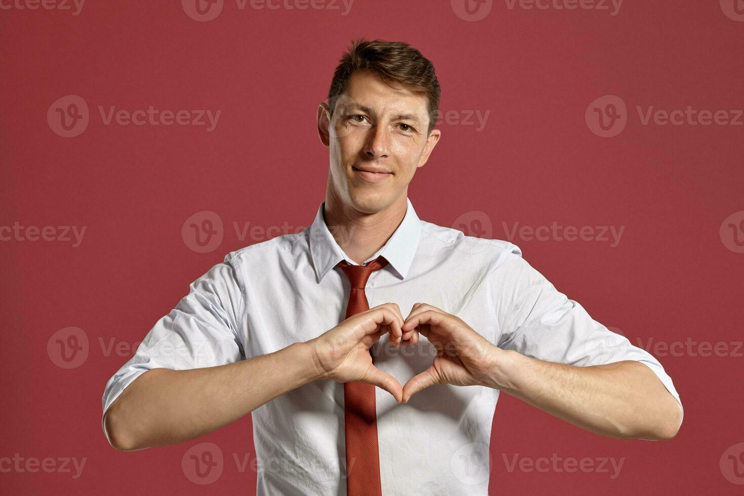 joven hombre en un clásico blanco camisa y rojo Corbata posando terminado un rosado antecedentes. foto