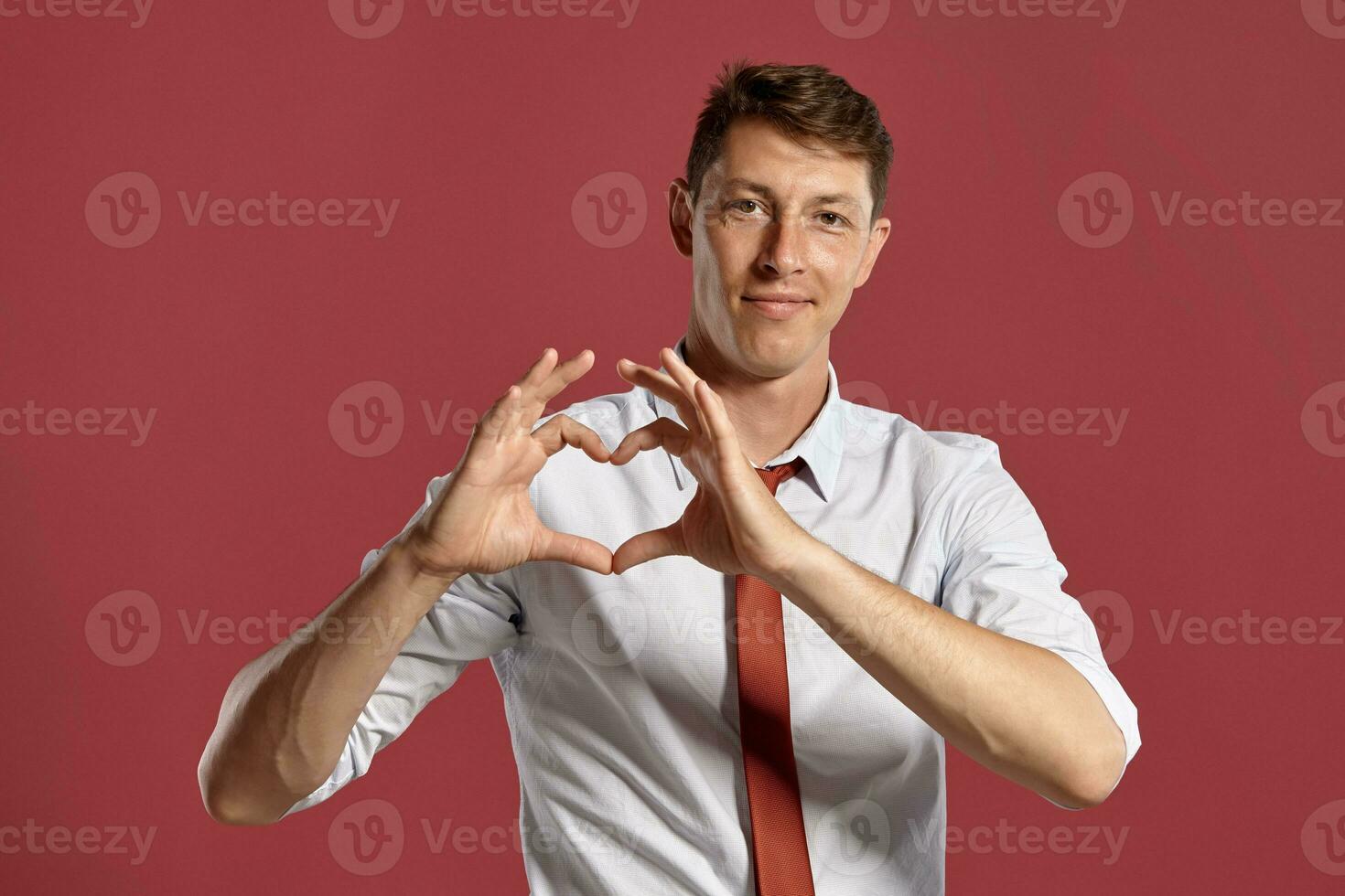 Young man in a classic white shirt and red tie posing over a pink background. photo