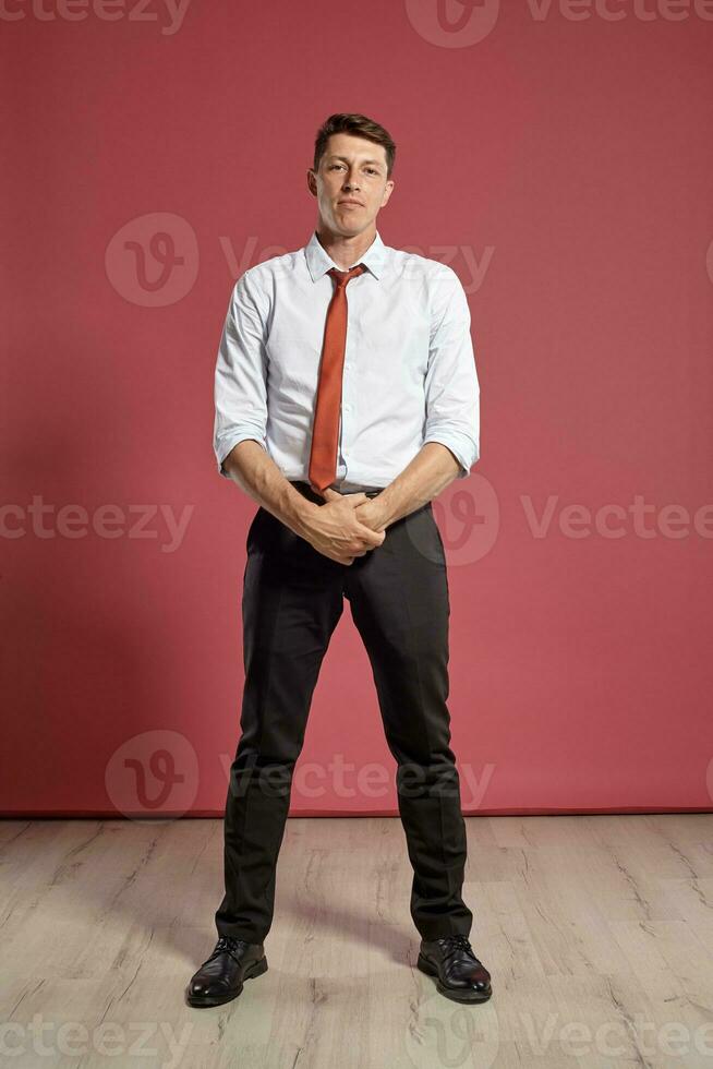 Portrait of a young brunet man posing in a studio against a red background. photo