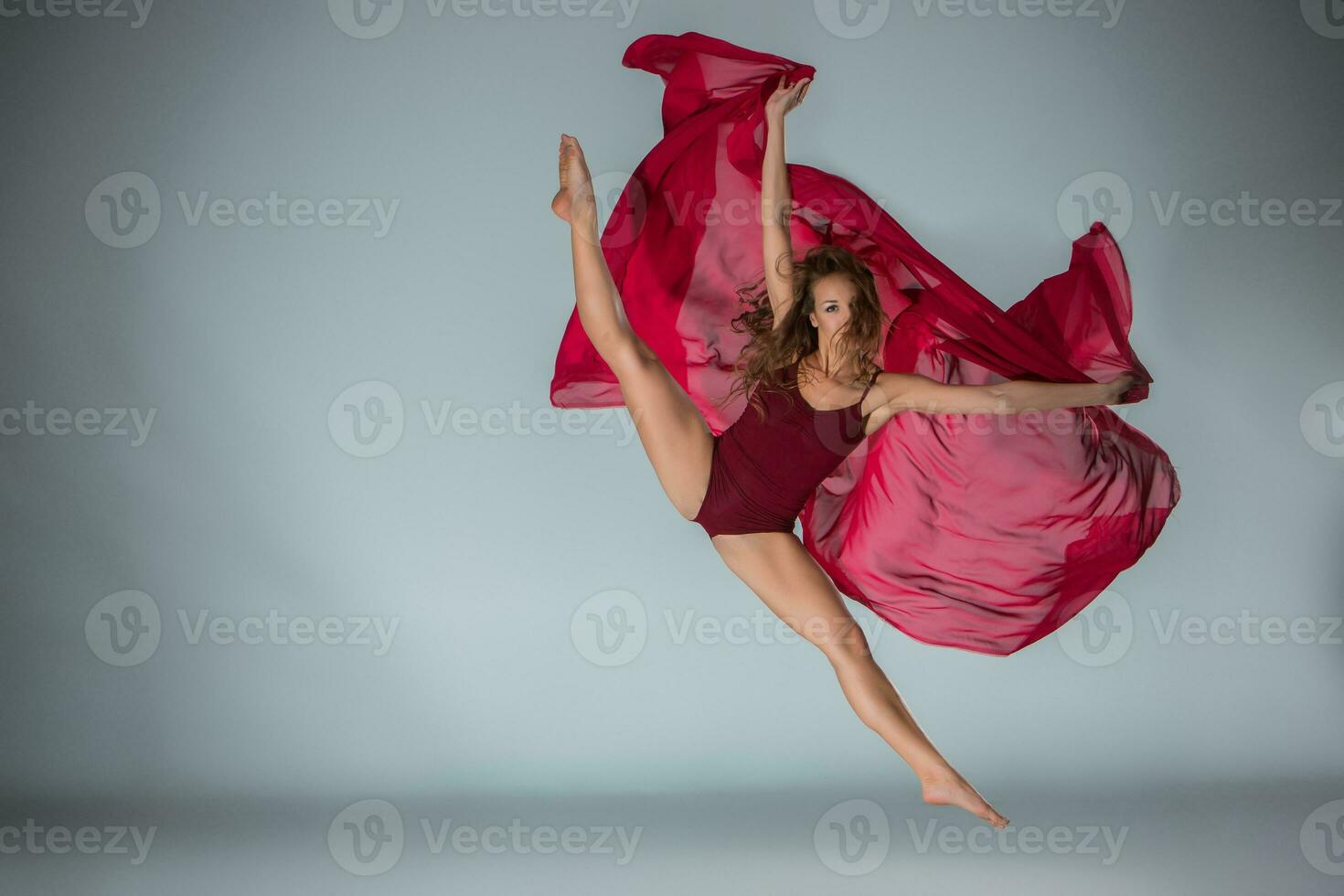 Young beautiful woman dancer in red swimsuit posing on a light grey studio background photo