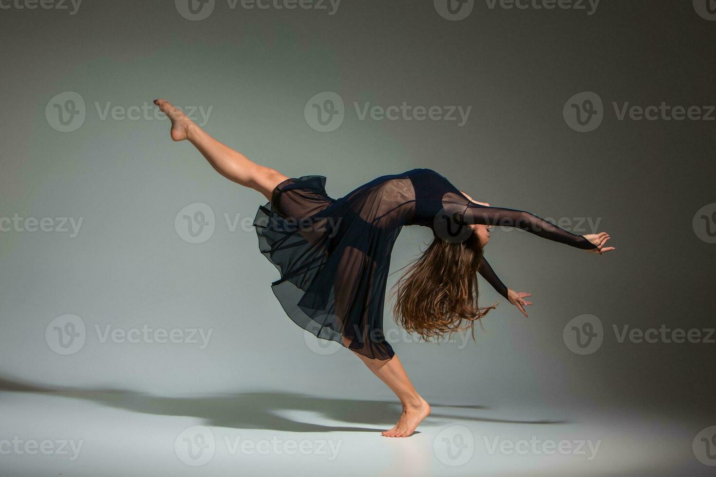 Young beautiful dancer in black dress posing on a dark gray studio background photo