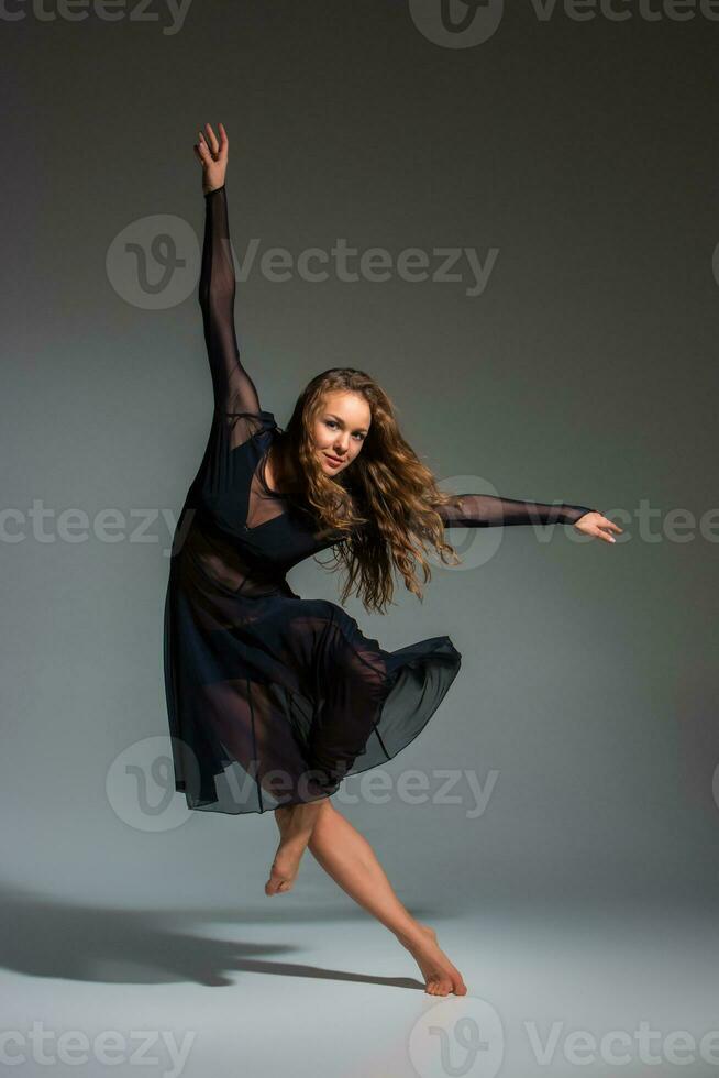 Young beautiful dancer in black dress posing on a dark gray studio background photo