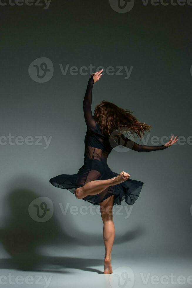 Young beautiful dancer in black dress posing on a dark gray studio background photo