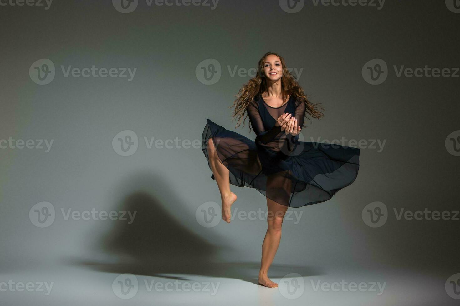 Young beautiful dancer in black dress posing on a dark gray studio background photo
