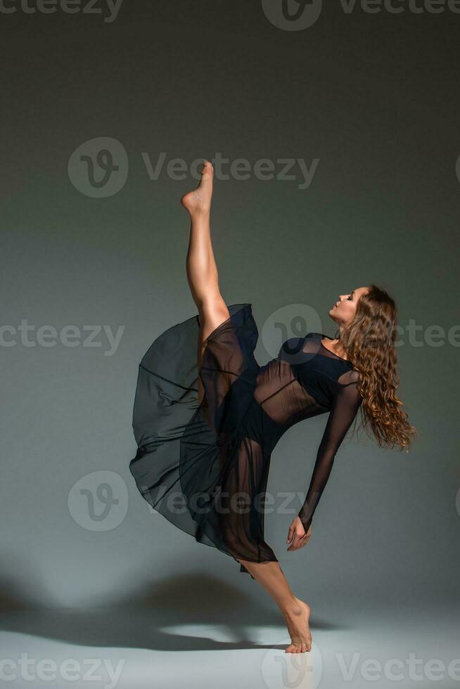 joven hermosa bailarín en negro vestir posando en un oscuro gris estudio antecedentes foto
