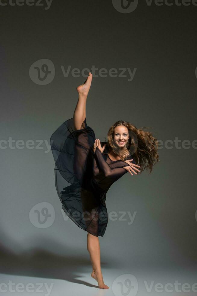 Young beautiful dancer in black dress posing on a dark gray studio background photo