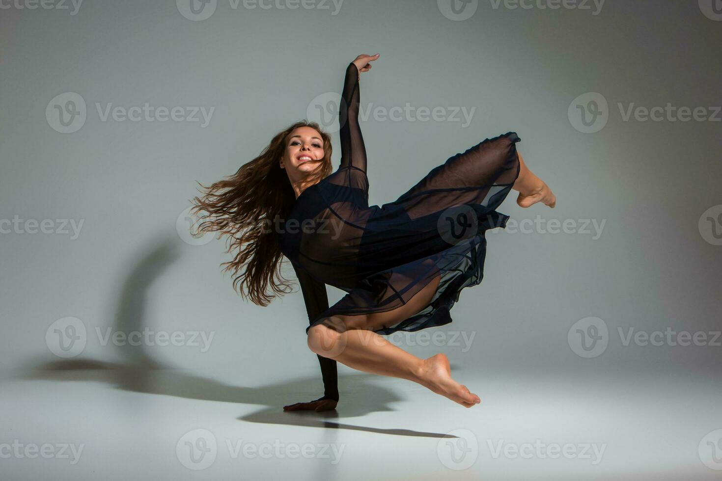 Young beautiful dancer in black dress posing on a dark gray studio background photo