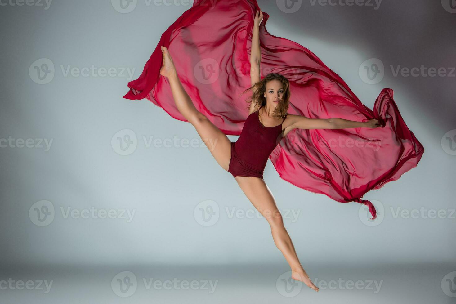 Young beautiful woman dancer in red swimsuit posing on a light grey studio background photo