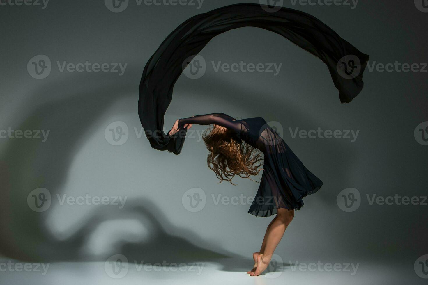 Young beautiful dancer in black dress posing on a dark gray studio background photo