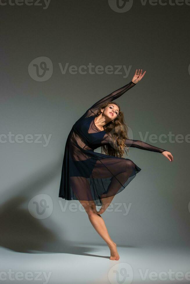 Young beautiful dancer in black dress posing on a dark gray studio background photo