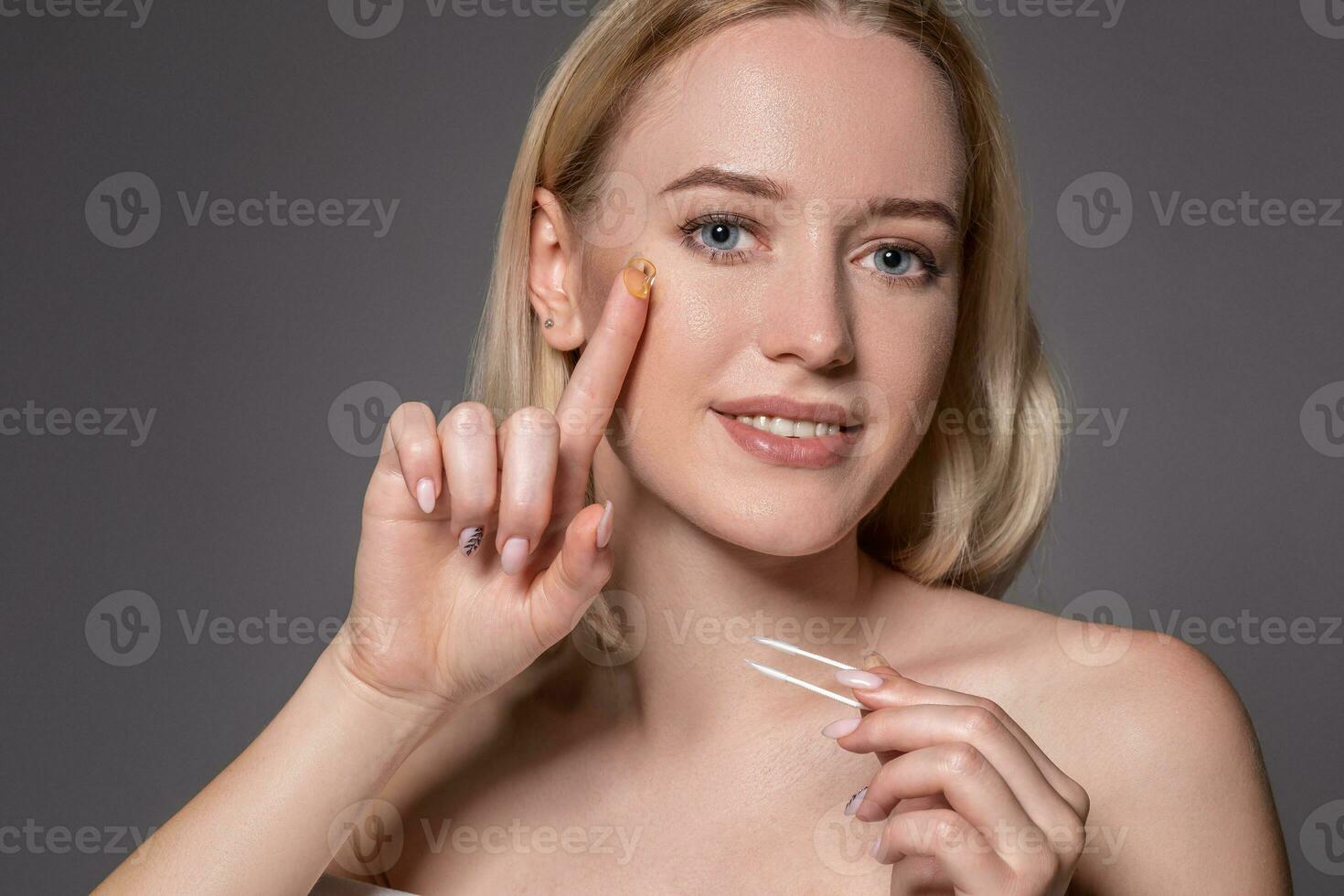 Portrait of young beautiful woman with natural makeup and contact eye lens in hand. Close-up of female model holding white tweezers for contact lenses. photo