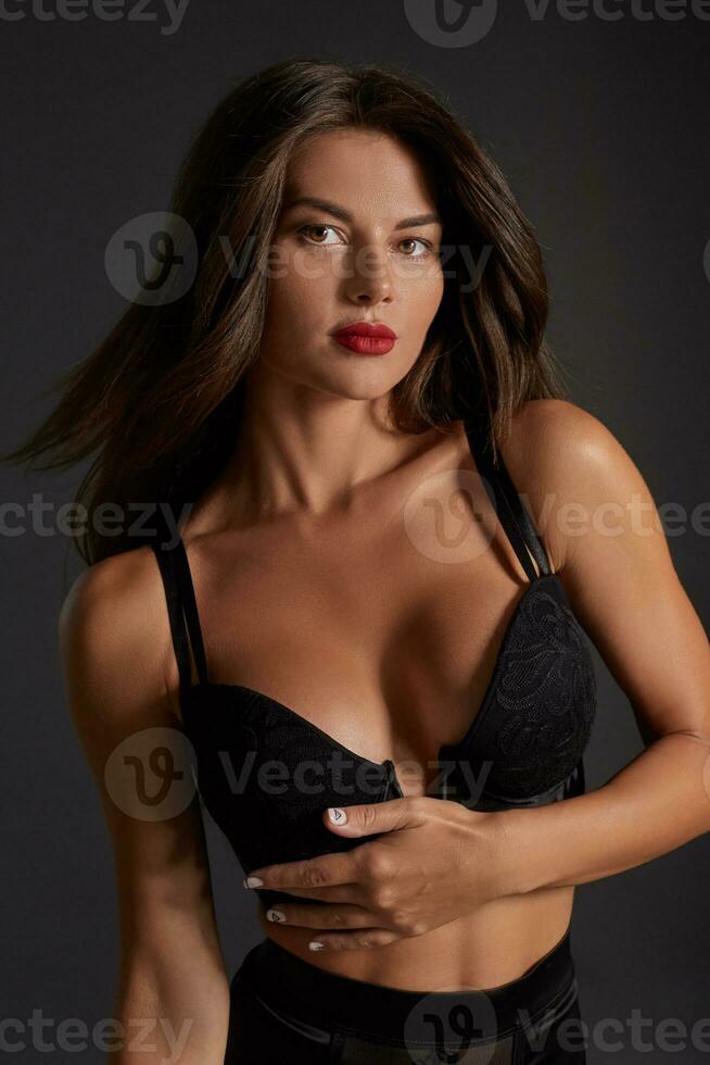 Stunning caucasian female model with dark hair and red lips in black underwear posing on dark grey background. photo