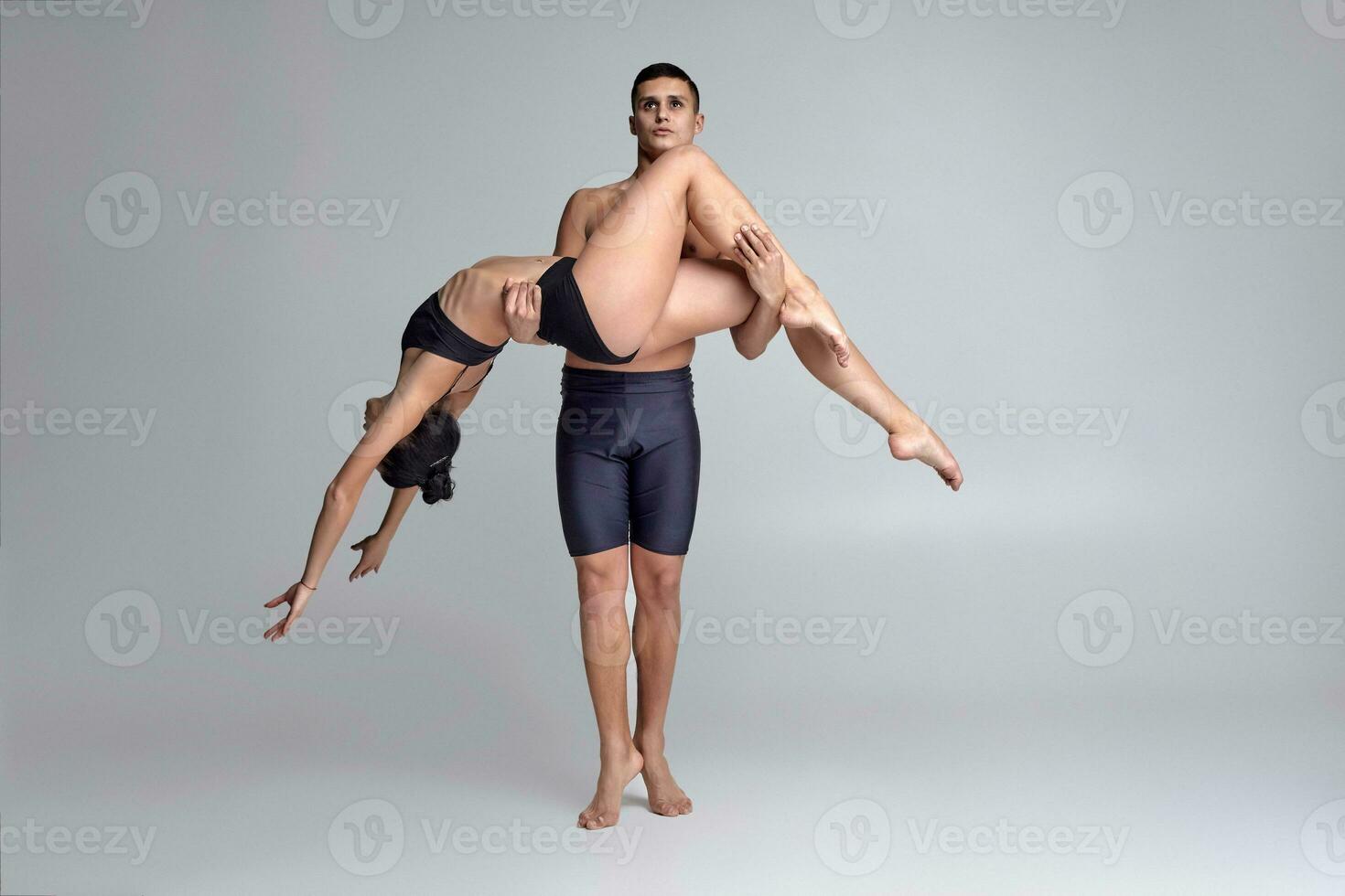 The couple of a young modern ballet dancers in black suits are posing over a gray studio background. photo