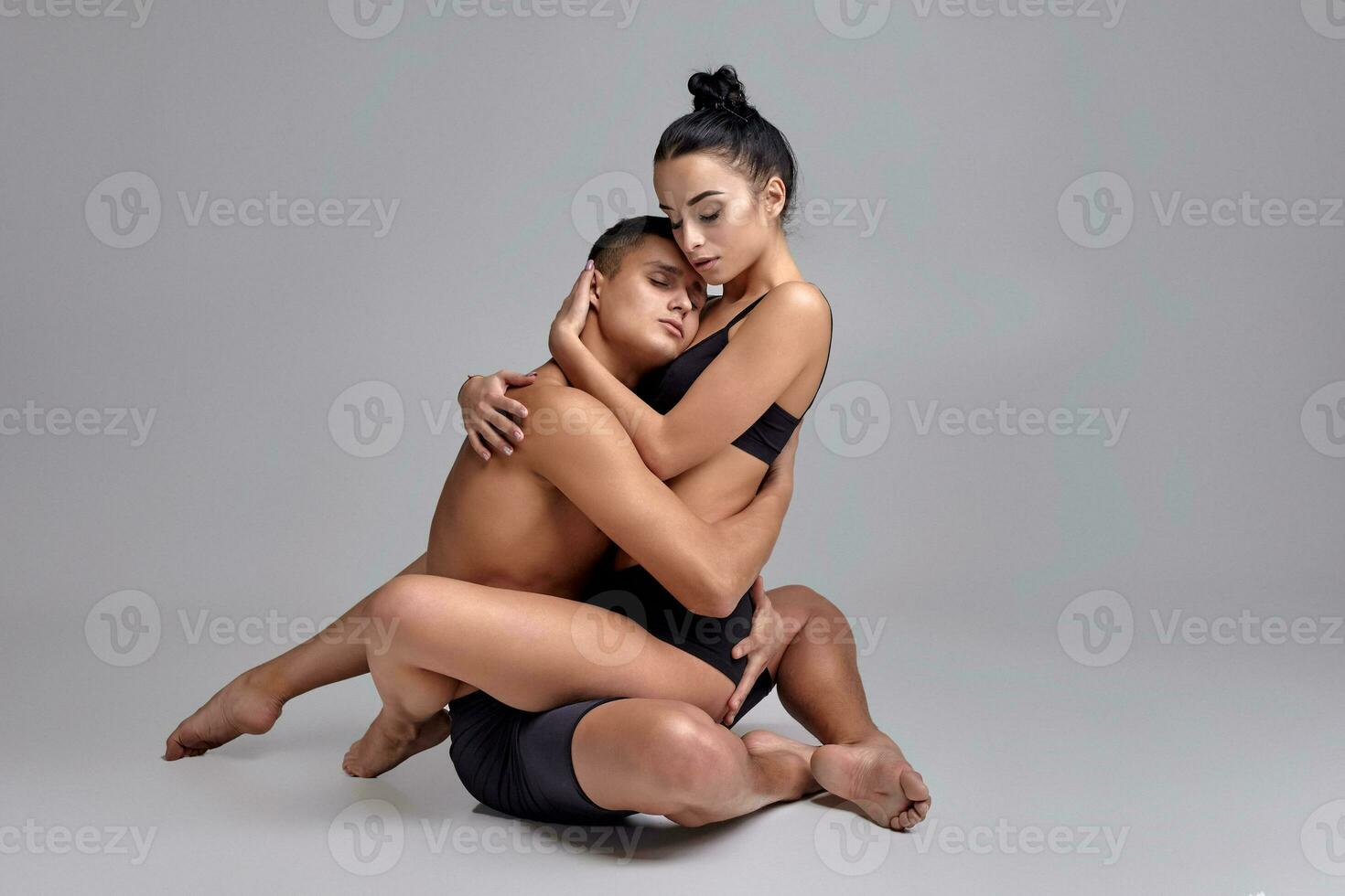 The couple of a young modern ballet dancers in black suits are posing over a gray studio background. photo