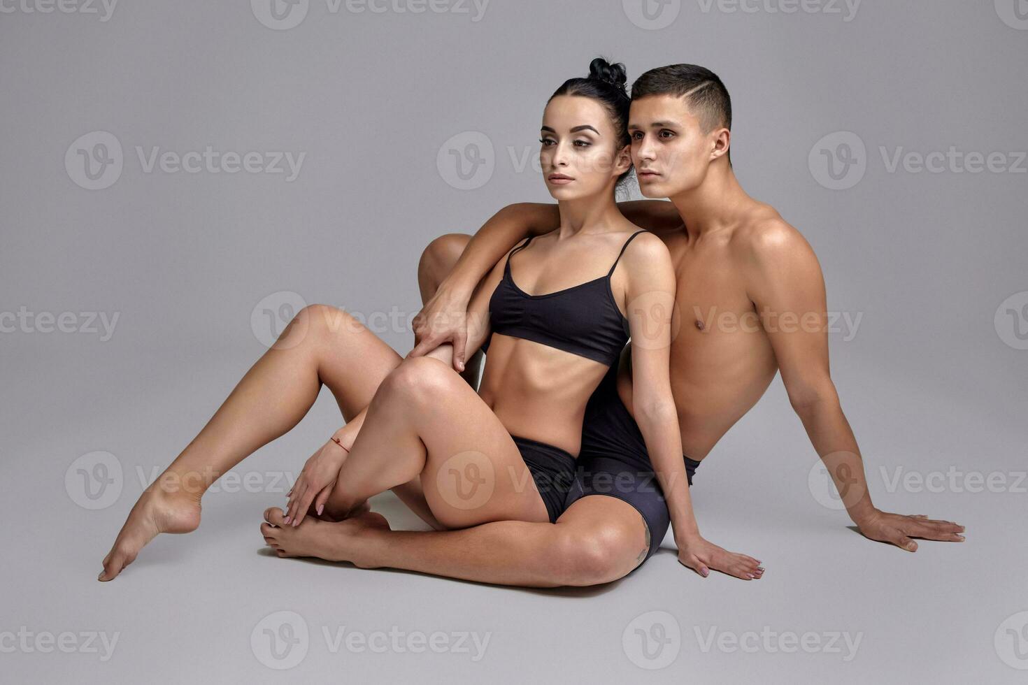 The couple of a young modern ballet dancers in black suits are posing over a gray studio background. photo