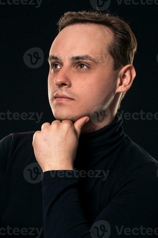 estudio Disparo de joven hombre mirando a el cámara en negro antecedentes. vertical formato, él tiene un grave rostro, él es vistiendo un negro pull-over. foto