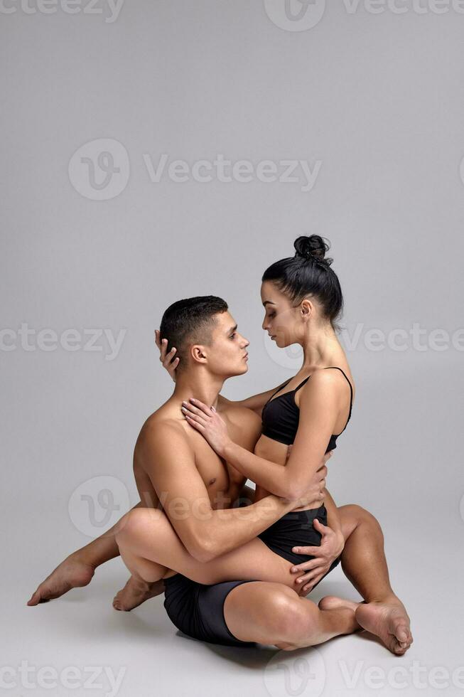 The couple of a young modern ballet dancers in black suits are posing over a gray studio background. photo