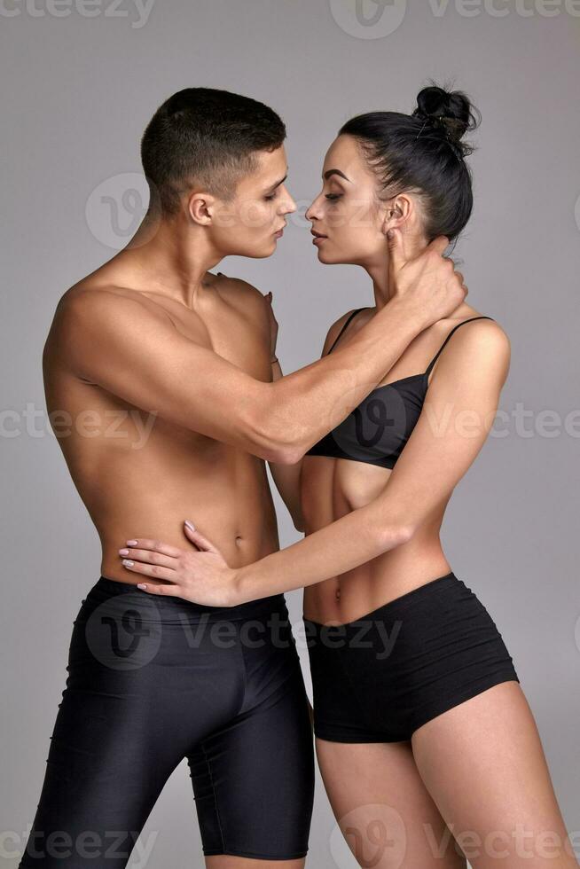 el Pareja de un joven moderno ballet bailarines en negro trajes son posando terminado un gris estudio antecedentes. foto