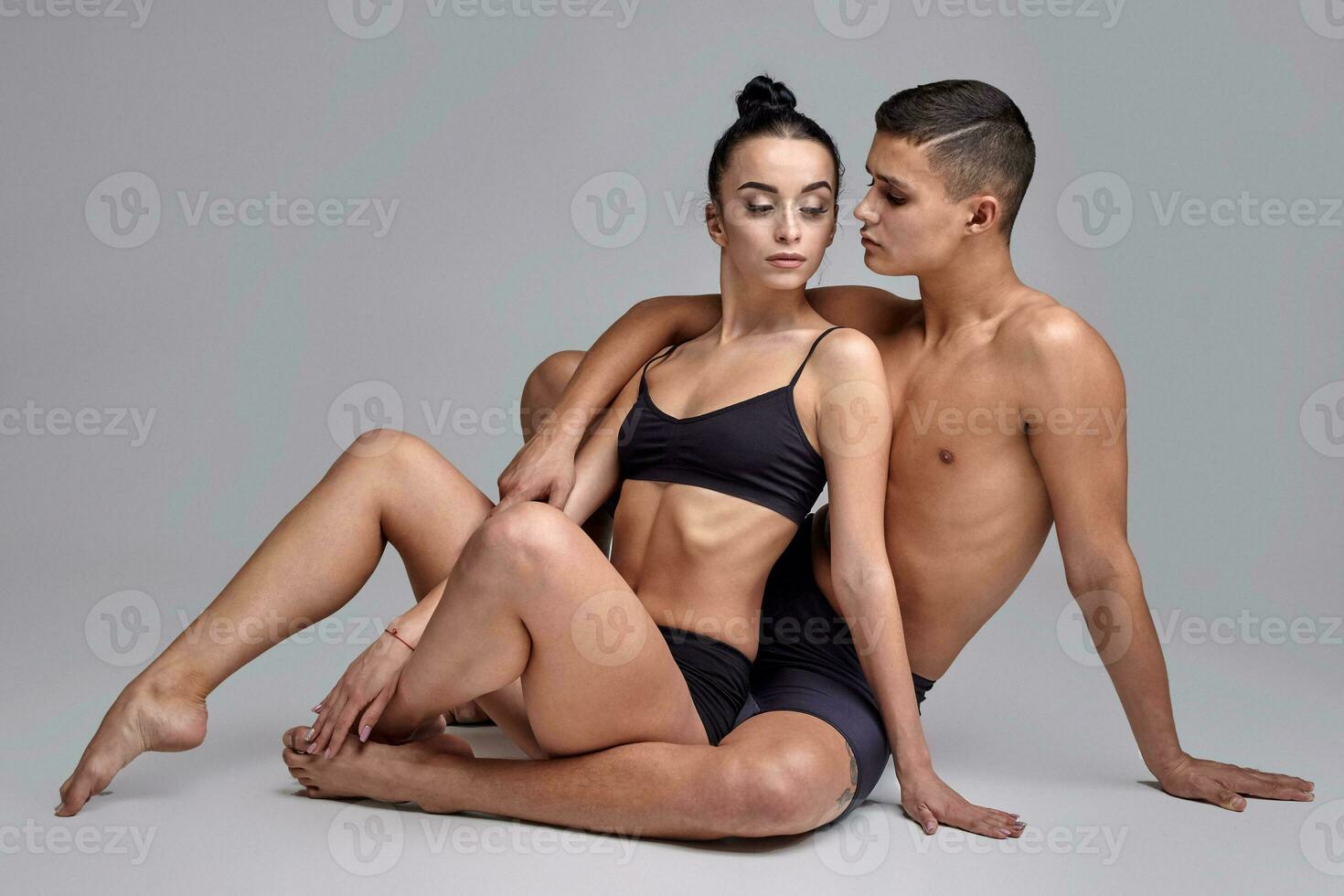 The couple of a young modern ballet dancers in black suits are posing over a gray studio background. photo