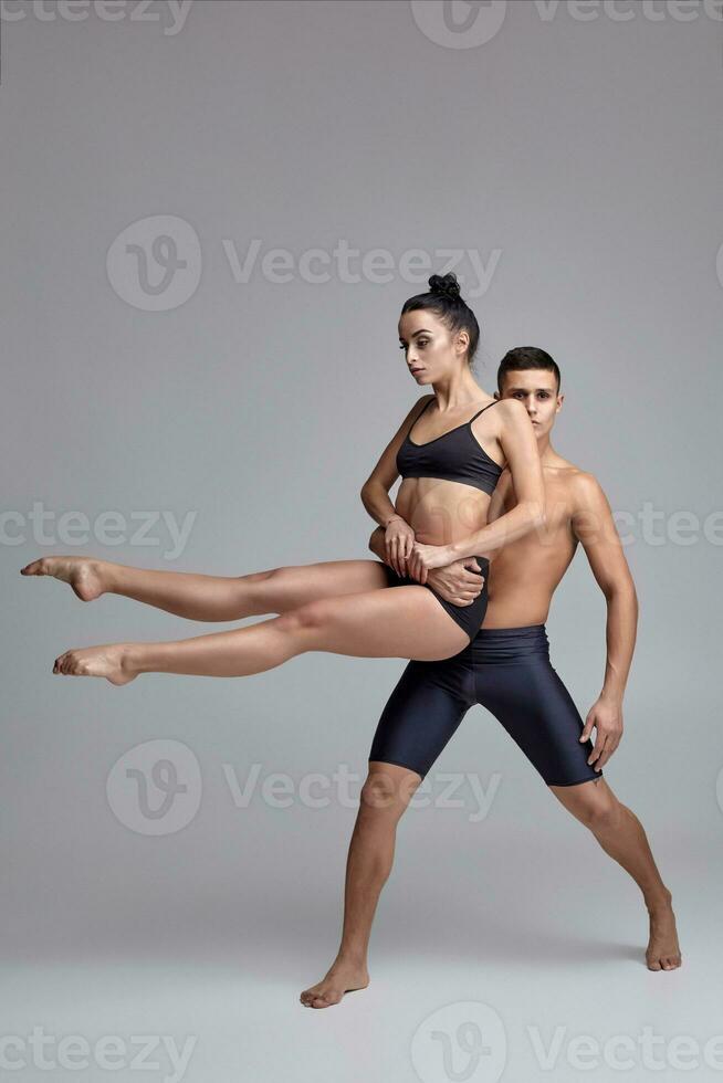 el Pareja de un joven moderno ballet bailarines en negro trajes son posando terminado un gris estudio antecedentes. foto