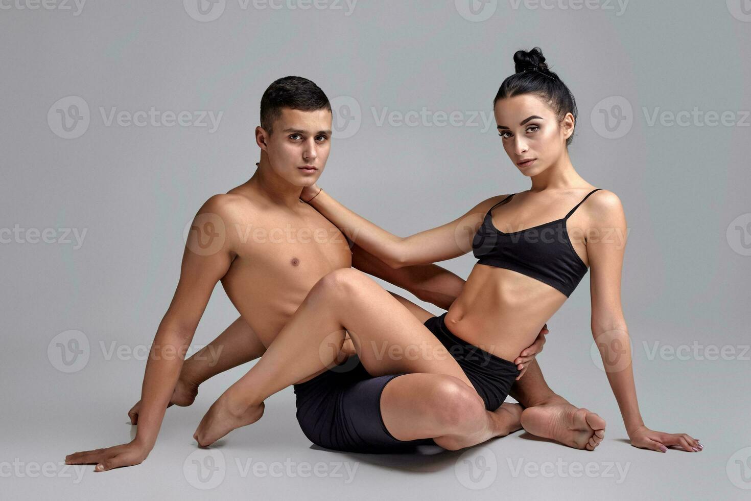 The couple of a young modern ballet dancers in black suits are posing over a gray studio background. photo