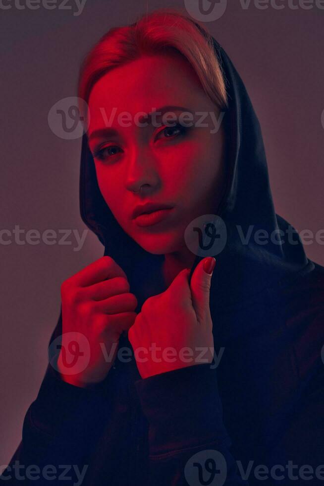 Young pretty woman wearing a black hood and shorts on dark background. Portrait photo