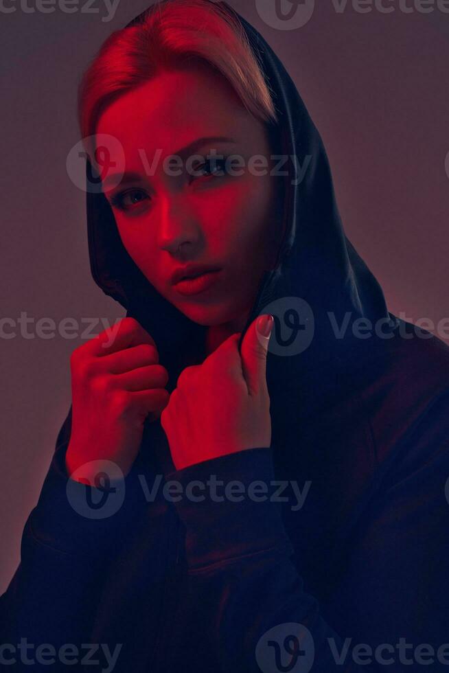 Young pretty woman wearing a black hood and shorts on dark background. Portrait photo