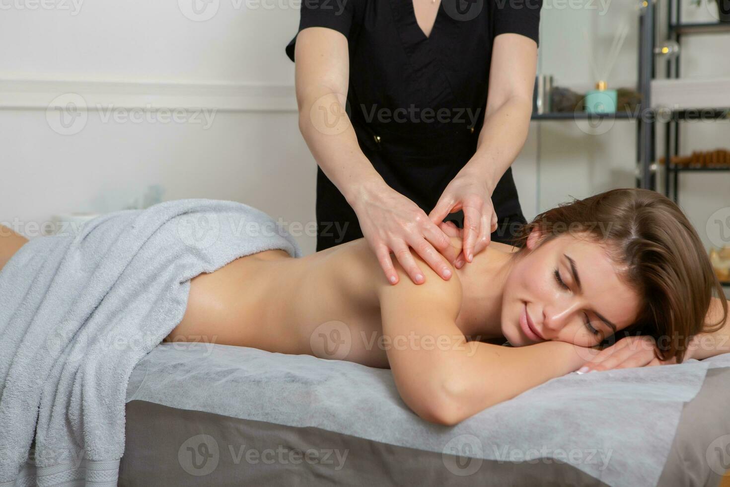 Professional masseur doing therapeutic massage. Woman enjoying massage in her home. Young woman getting relaxing body massage. photo