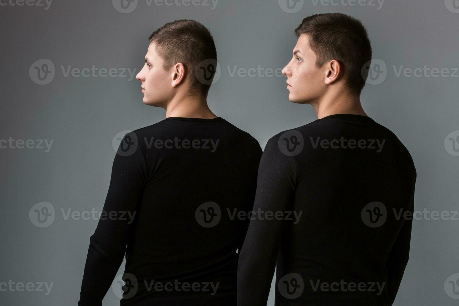 The two twin brother stand with their backs on the gray backgrou photo