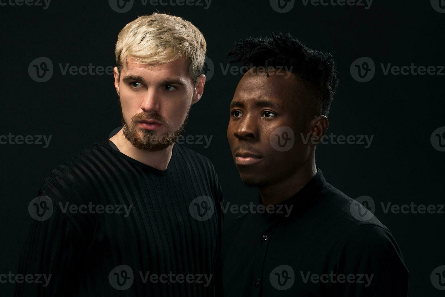 Portrait of two young african american and caucasian men standing over black background. Studio shot photo