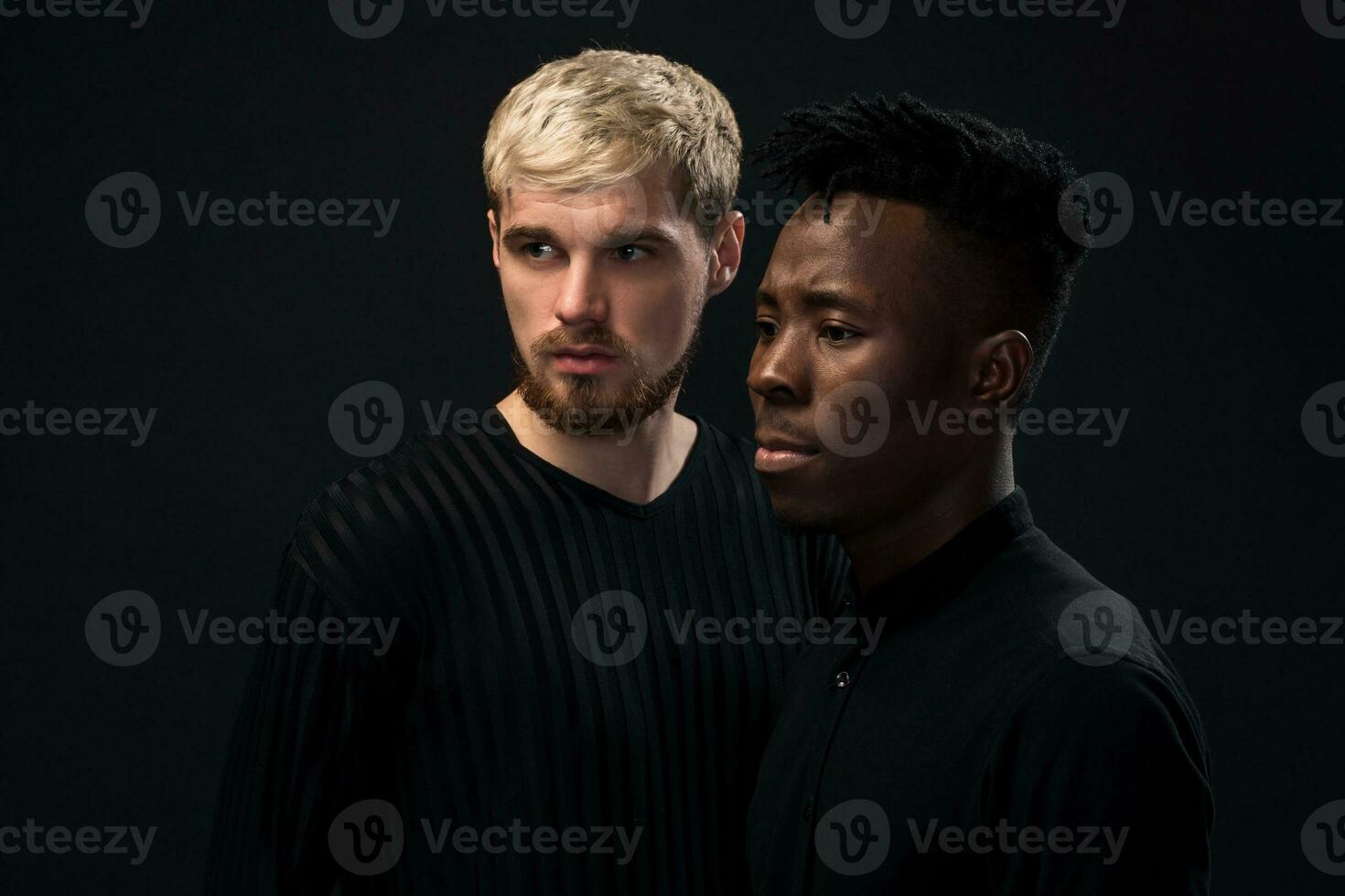 Portrait of two young african american and caucasian men standing over black background. Studio shot photo