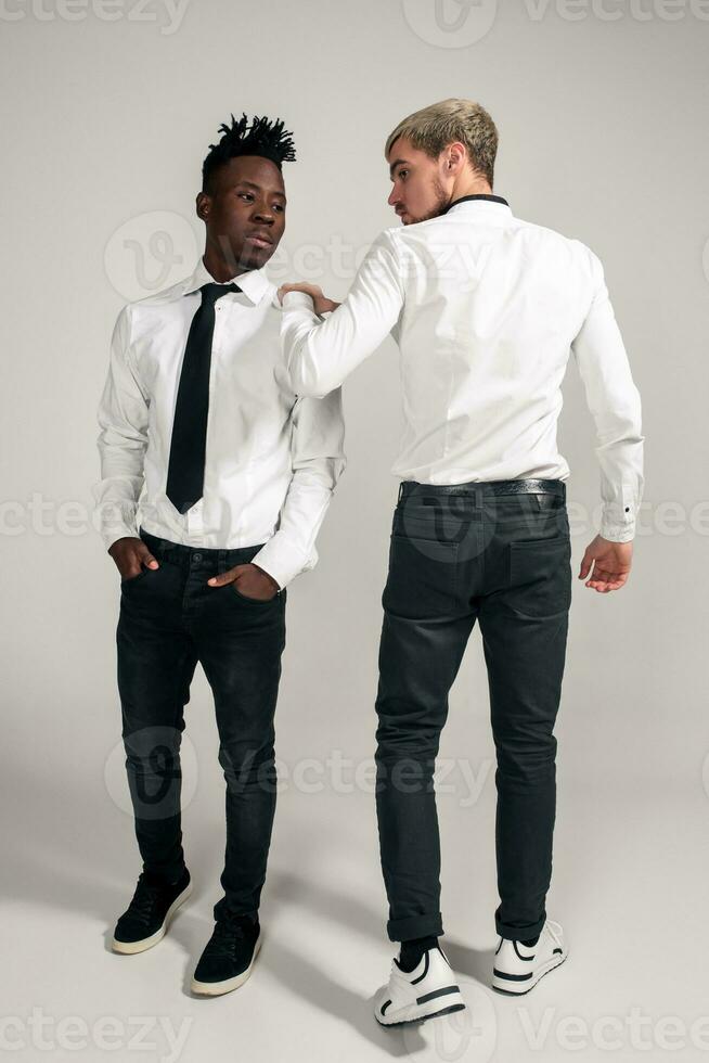 Joyful relaxed african and caucasian boys in white and black office clothes laughing and posing at white studio background with copy space photo