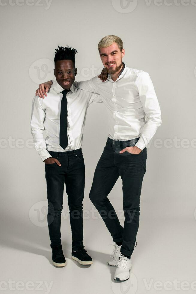 Joyful relaxed african and caucasian boys in white and black office clothes laughing and posing at white studio background with copy space photo