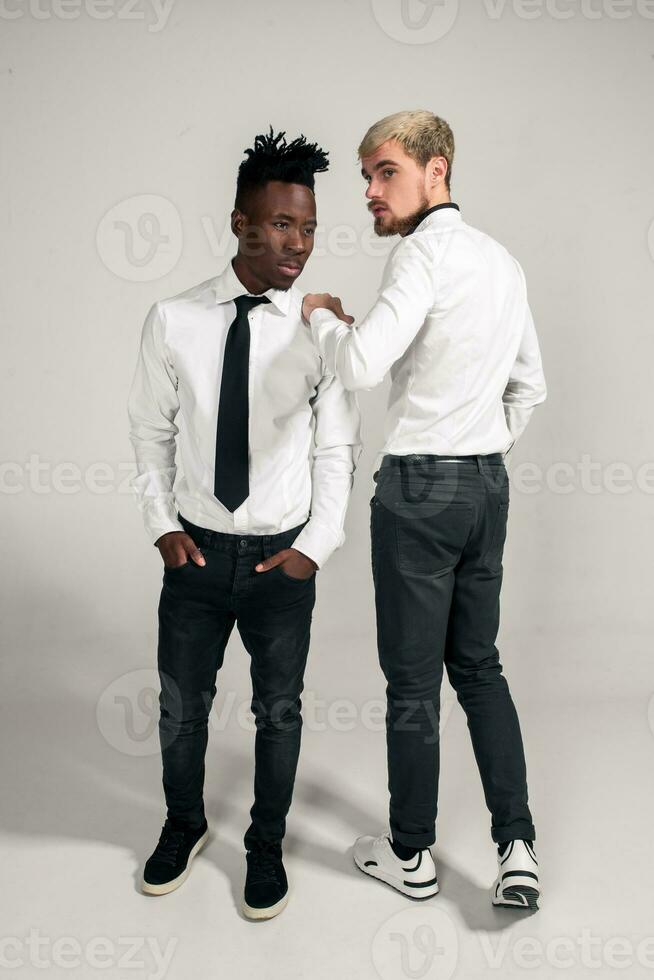 Joyful relaxed african and caucasian boys in white and black office clothes laughing and posing at white studio background with copy space photo