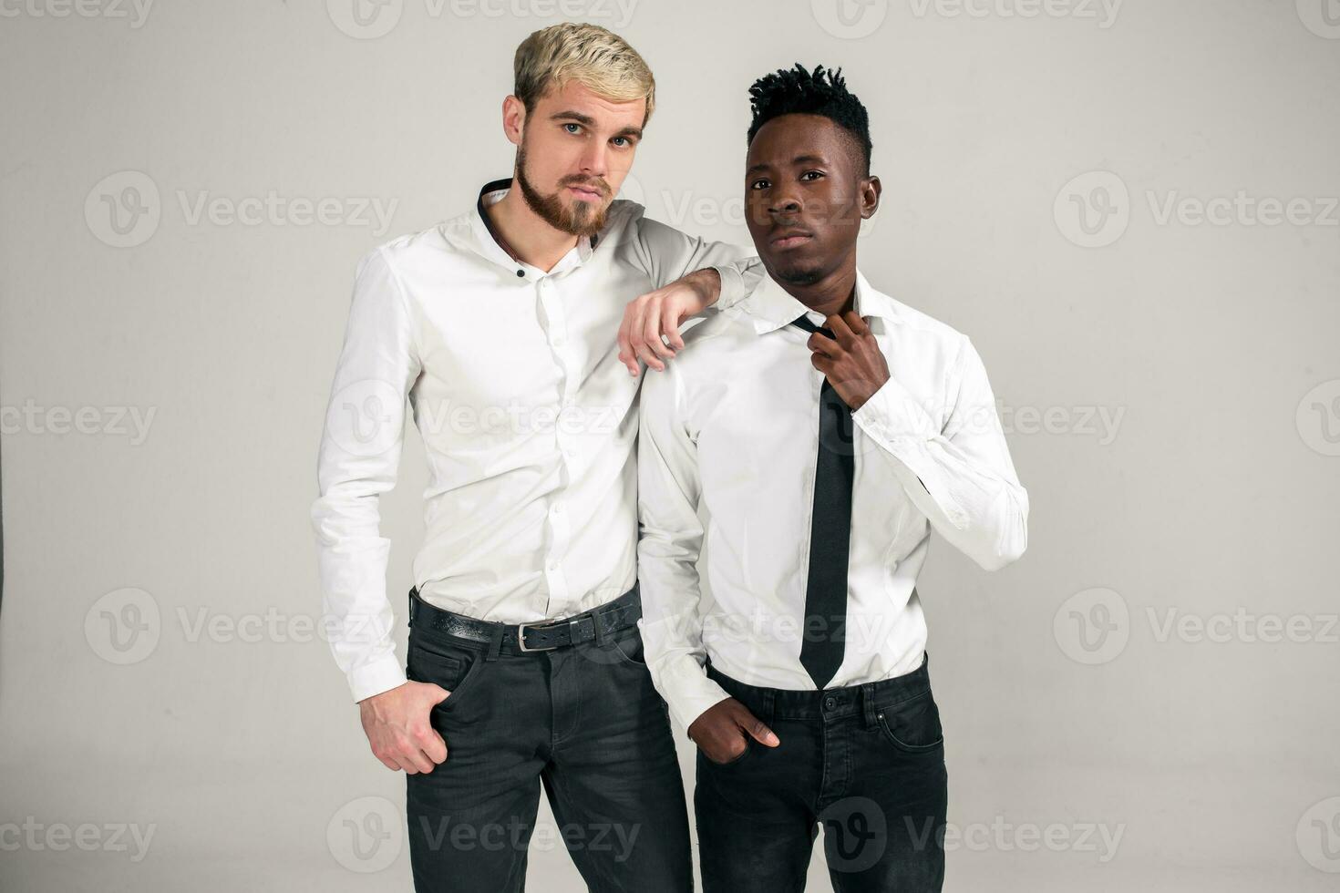 Joyful relaxed african and caucasian boys in white and black office clothes laughing and posing at white studio background with copy space photo