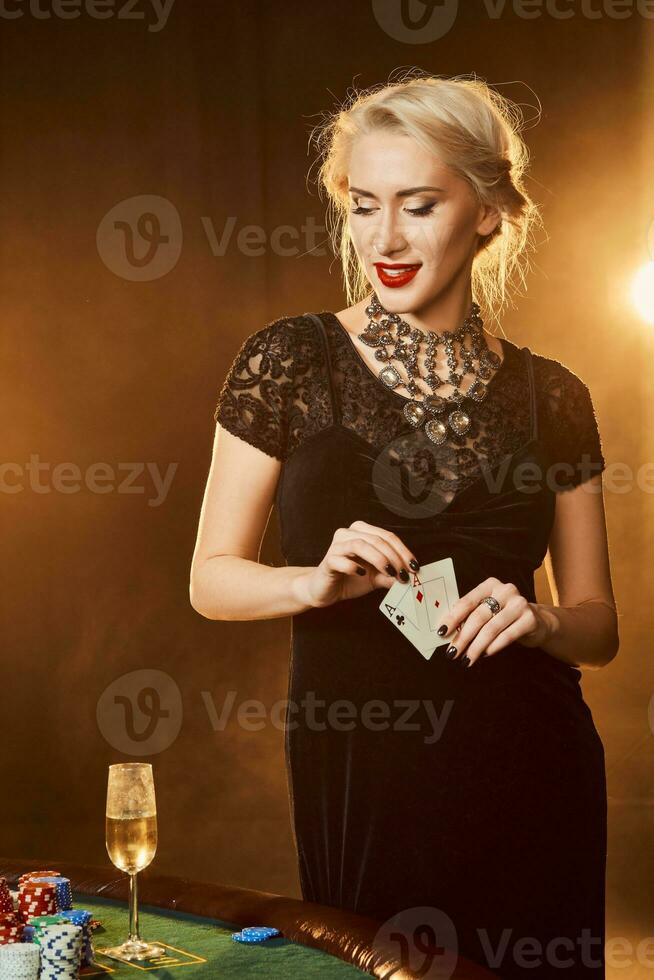 A woman in a black dress with cards in her hands is standing near the poker table photo