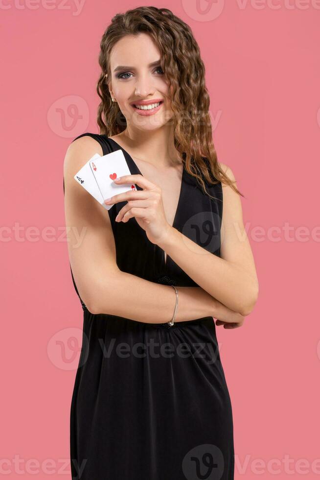 Young woman holding two aces in hand against on pink background photo