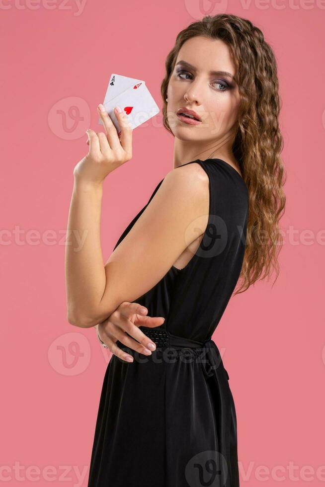 Young woman holding two aces in hand against on pink background photo